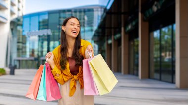 Alışveriş zamanı. Alışveriş merkezinin önünde elinde poşetlerle dolaşan mutlu bir kadın. Tüketim, alım, mevsimlik satış kavramı