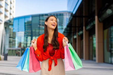 Alışveriş neşesi. Elinde bir sürü kese kâğıdı olan bayanın dışarıda durup alışveriş paketlerini heyecanla göstermesi.
