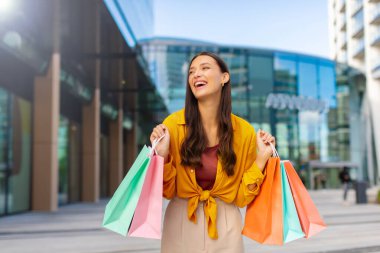 Alışveriş neşesi. Elinde bir sürü kese kâğıdı olan bayanın dışarıda durup alışveriş paketlerini heyecanla göstermesi.