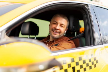 Pozitif özenli orta yaşlı taksi şoförü. Sarı araba kullanıyor. Açık camlı aynaya bakıyor.