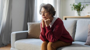 Evdeki kanepede oturan düşünceli yaşlı kadın, uzaklara bakıyor ve düşüncelerinde kaybolduğunu düşünüyor, yalnız hissediyor, panorama, boş alan