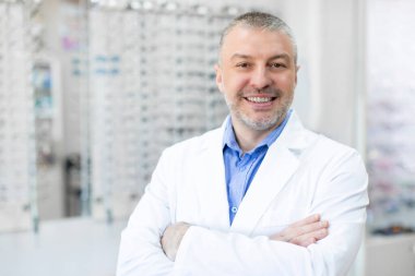 Optik dükkanında çalışan, kollarını kavuşturup kameraya gülümseyen orta yaşlı bir adamın portresi. Göz konsepti