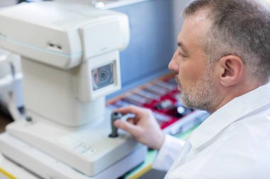 Modern klinikteki hastanın göz vizyonunu kontrol eden profesyonel erkek doktor, modern oftalmolojik cihaz kullanıyor.