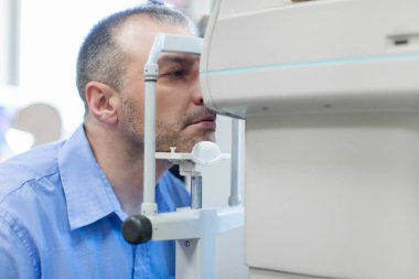 Orta yaşlı bir adam otomatik fraktometre ekranında görme yeteneğini inceliyor. Gözlerin yansıma yeteneğini analiz etmek ve uygun düzeltici maddenin seçimini kolaylaştırmak için optalmik aygıt