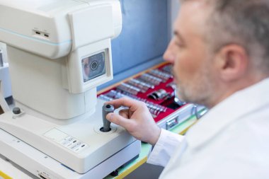 Profesyonel erkek göz doktoru klinikte modern göz hekimliği cihazıyla göz muayenesi yapıyor.