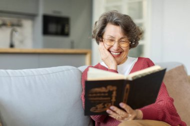 Heyecanlı, gözlüklü, kanepede dinlenen kitap okumaktan, evde boş vakit geçirmekten, fotokopi çekmekten hoşlanan yaşlı kadın.