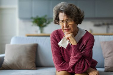 Üzgün yaşlı bayan ağlıyor, düşüncelere ve anılara dalmış, yaşlı kadın kendini yalnız ve terk edilmiş hissediyor, peçete tutuyor, evdeki koltukta oturuyor.