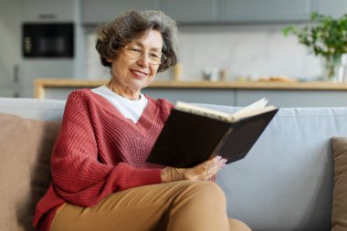 Pozitif kıdemli kadın emekliliğin tadını çıkarıyor, kanepede oturuyor ve kitap okuyor, boş yer var.