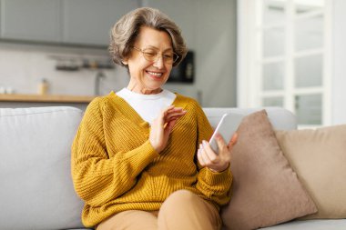 Harika bir teklif. Mutlu, modern, son sınıf öğrencisi bir kadın elinde akıllı bir telefonla kanepede dinleniyor. İnternette gülümsüyor ve mesajlaşıyor.
