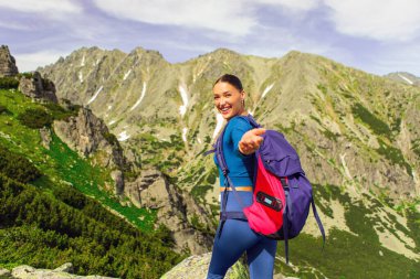Kadın gezgin tepenin üstünde duruyor ve kameraya doğru gülümsüyor, güzel doğanın tadını çıkarıyor.