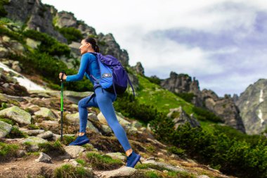 Güneşli bir yaz günü dağlarda yürüyüş yapan, sırt çantası takan ve yürüyüş direkleri kullanan, fotokopi çeken genç bir kadın.