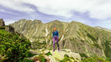 Kadın gezginin, dağların tepesinde güneşli bir yaz gününde manzaranın tadını çıkardığı uzun bir çekim.