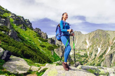 Yürüyüş direkleri ve sırt çantasıyla gezen mutlu kadın turist, üstünde duruyor ve manzaranın tadını çıkarıyor. Eğlence, yeşil turizm ve aktif yaşam tarzı