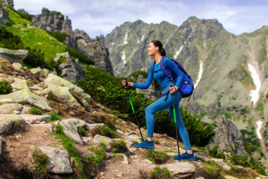 Dağın tepelerinde çubuklarla gezen bayan gezgin aktif bir hayat sürüyor ve güzel manzaraların tadını çıkarıyor.