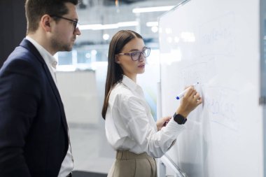 Profesyonel iş kadını beyaz tahtaya yazı yazıyor ve sunumdan önce erkek arkadaşına raporunu açıklıyor.