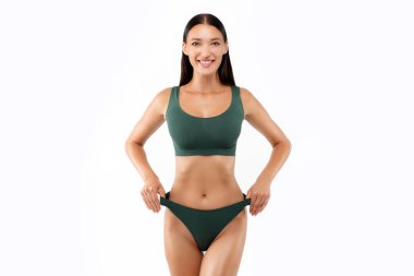 Yeşil iç çamaşırı giyen sağlıklı bir kadının portresi, beyaz stüdyo arka planında tek başına duran, iç çamaşırlı ve iç çamaşırlı ince bir kadın.