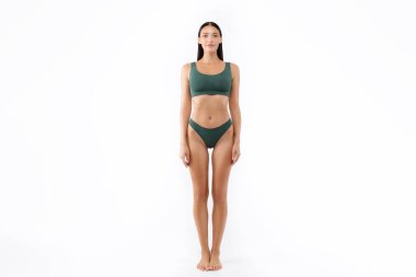 Beyaz stüdyo arka planında poz veren, yeşil iç çamaşırı giyen mükemmel vücutlu genç bir kadının ön görüntüsü.