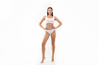 Beyaz iç çamaşırı ve külotla beyaz stüdyo arka planında poz veren güzel bir kadının uzun pozu güzel kıvrımlar gösteriyor.