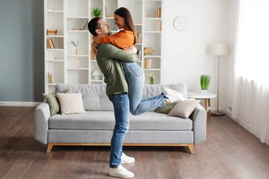 Sevgili karısını kucağında tutan ve kucaklayan genç bir adam. Oturma odasında dikilen bir çift. Eşler sevgi ve sevgiyi ifade eder