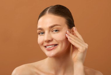 Göz bakımı konsepti. Mutlu güzel bayan kumaş göz bandı takıyor ve gülümsüyor, bej arka planda poz veriyor.