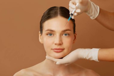 Alnına enjekte edilen genç bir kadının portresi beyaz eldiven giyen, kahverengi arka planda tıp uzmanı bir kozmetikçiden.