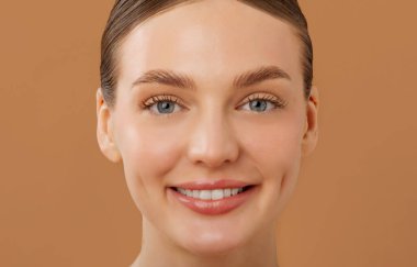 Mükemmel parıldayan derisi olan güzel Avrupalı bir kadının, bej arka planda izole edilmiş bir şekilde kameraya baktığı yakın plan fotoğrafı.