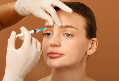 Kadın glabella yüz gençleştirme prosedürü için hyaluronik asit enjeksiyonu yaptırıyor, kaş aralarında kozmetik enjeksiyon yaptırıyor.
