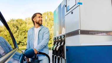 Araba yakıtı teklifi. Benzin istasyonunda benzin dolduran yakışıklı adam benzin makinesi, panorama ve boş alana bakıyor.