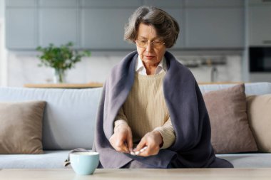 Hasta, gri saçlı, hap alan, evinde battaniyeye sarılmış, kendini kötü hisseden yaşlı bir kadın.