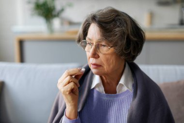 Tedavi, emeklilikte ilaç. Hap alan yaşlı bir kadın, ağzının kenarında ilaçla el ele tutuşan yaşlı bir bayan, yakın çekim.