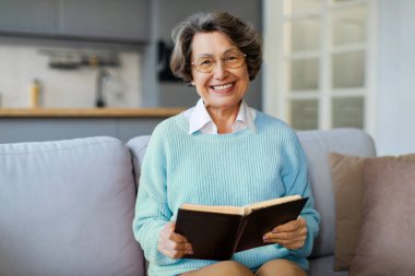 Rahat, mutlu, kağıt kitap okuyan, rahat bir koltukta oturan, ilginç edebiyattan hoşlanan, hafta sonu evde dinlenen, son sınıf öğrencisi bir kadın.