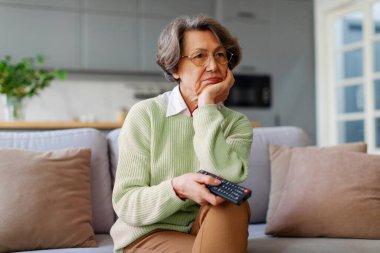 Elinde uzaktan kumandayla evde oturan üzgün yaşlı bir kadın. Sıkılmış, TV 'de izleyecek ilginç bir şeyler arıyor.