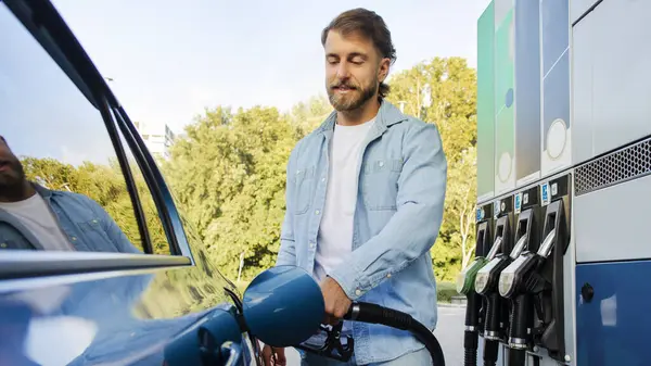 Otomobil yakıt ikmali teklifi. Modern benzin istasyonunda otomobili biyo yakıtla dolduran yakışıklı adam, panorama çekimi, pankart