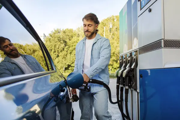 Yakışıklı Avrupalı bir adam benzin istasyonunda arabasına yakıt dolduruyor, benzin deposunda mazot dolduruyor.
