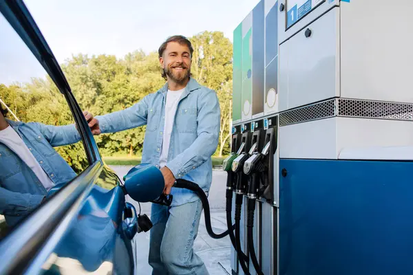Benzin istasyonunda yakıt ikmali yapan mutlu Avrupalı bir adam. Yakıt hortumunu tutuyor ve kameraya gülümsüyor. Dışarıda otomobilin yanında duruyor. Benzin kavramı
