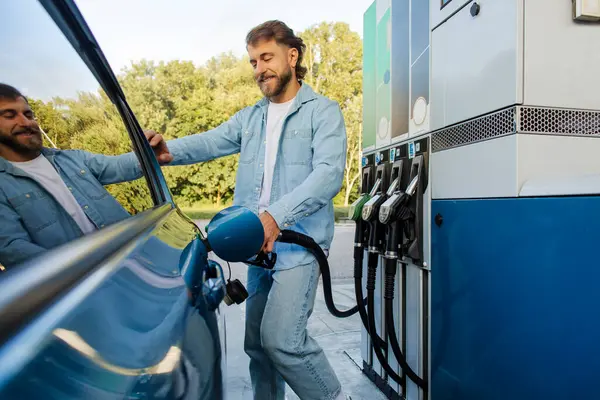 Çevre dostu yakıt ikmali. Modern benzin istasyonunda adam otomobili biyo yakıtla dolduruyor, arabanın yanında duruyor ve silah hortumunu tutuyor.