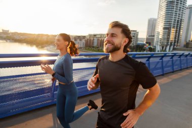 Sabah sporu. Hızlı atlet Avrupalı kadın ve erkek birlikte şehir köprüsünde koşuyorlar, açık havada spor eğitimi alıyorlar.