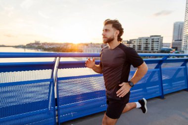 Güçlü koşucu dışarıda antrenman yapıyor, yaya köprüsünde koşuyor, dışarıda akşam antrenmanı yapıyor, boş yer var.