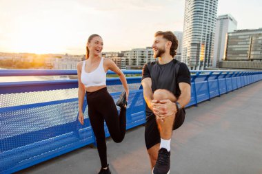 Fit bir adam ve kadın bacaklarını yaya köprüsünde açıyorlar, akşam koşusundan önce ısınıyorlar.