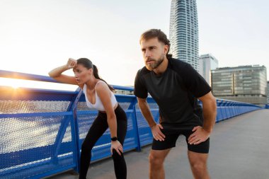 Yorgun genç çift koşucuları dışarıda sıkı çalıştıktan sonra nefes alıyorlar, dinleniyorlar, şehir köprüsünde duruyorlar.