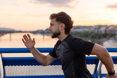 Gün batımında şehir köprüsünde koşarken müzik dinleyen genç bir atlet. Fitness ve sağlıklı yaşam tarzı.