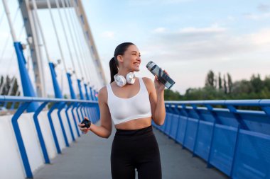 Sportif bayan koşup akşamları dışarıda antrenman yaptıktan sonra dinlenip su içiyor. Boşluğu kopyalayın.