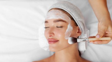 Mükemmel bir fırça dokunuşu. Güzellik salonunda, panoramada, boş alanda uzanan temiz cilt için rahatlatıcı kozmetik maskeli güzel bir bayan.