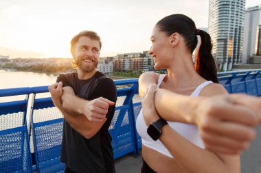 Spor yapan sporcu çift, antrenman başlamadan önce ısınıyor, spor giyimli kadın ve erkek antrenmana hazırlanıyor, şehir köprüsünde duruyor.
