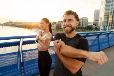 Eşler aktif ve sağlıklı bir hayat sürüyorlar, koşmadan önce kardiyo fitness için ısınıyorlar, açık havada antrenman yapıyorlar, şehir köprüsünde duruyorlar.
