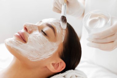 Yüz güzelliği tedavisi. Kaplıca salonunda kozmetik maske takan bir kozmetik uzmanı. Kapanış. Cilt bakımı kavramı