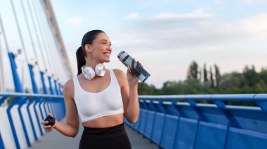 Koştuktan ve açık havada antrenman yaptıktan sonra deniz kenarındaki gezinti alanında dinlenen ve içen Avrupalı bir kadın, panorama, kopyalama alanı