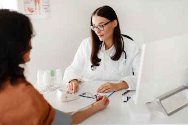 Doktor, kadın hastaya kan sayımı monitörü takıyor, tıbbi teşhis koyuyor, klinikte hastalık tedavisi uyguluyor.