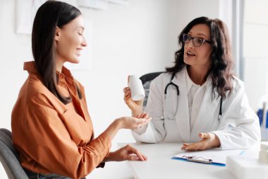 Klinikte kontrol ettikten sonra genç bayan hastaya reçete yazan gülümseyen doktor kadın, elinde haplı bir kavanoz tutan doktor.