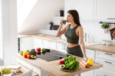Yeşil sebzelerden yapılmış smoothie içen genç, formda bir kadın, her sabah mutfakta durup, sağlıklı içeceklerin ve bedava alanların tadını çıkarıyor.